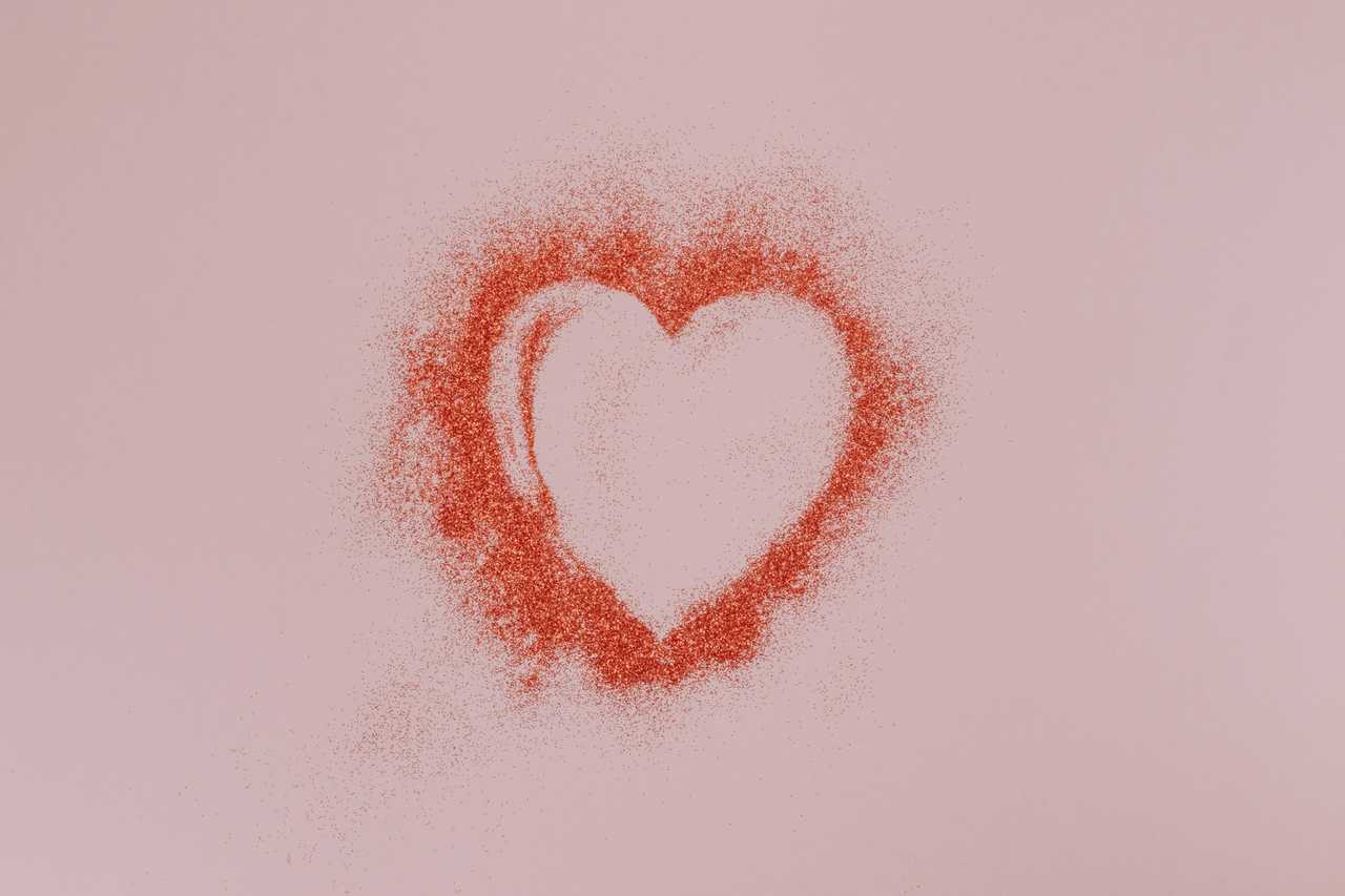 heart drawn with glitter and red colored dust in a pink paper for a love confession gesture
