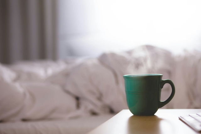 fumigating cup of coffee in a desk by a bed with good morning messages bed with sheets in the background
