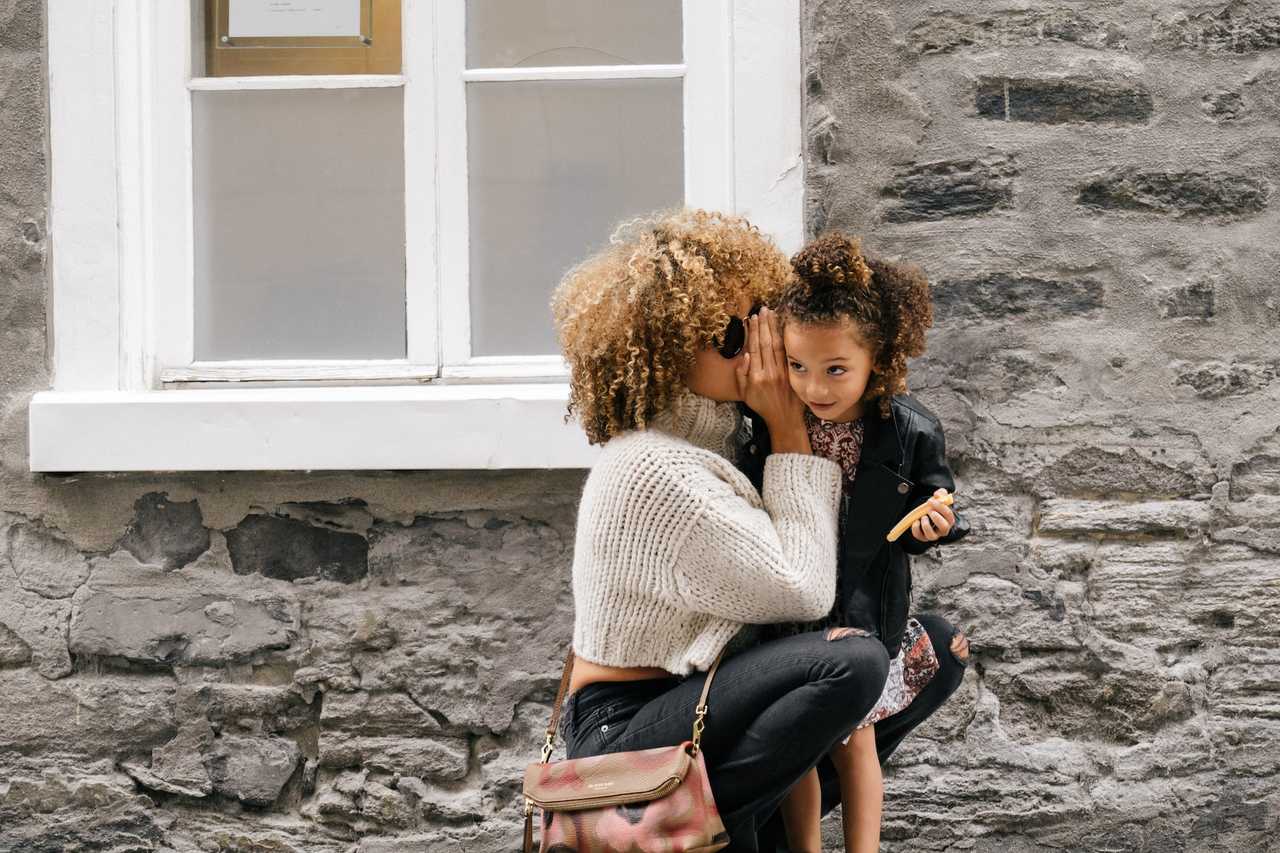 mother holding kid saying somehting in her ear after getting happy mother's day wishes