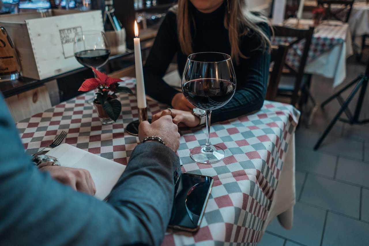 detail of a date with the couple holding hands on their first date glass of wine and candle over the table