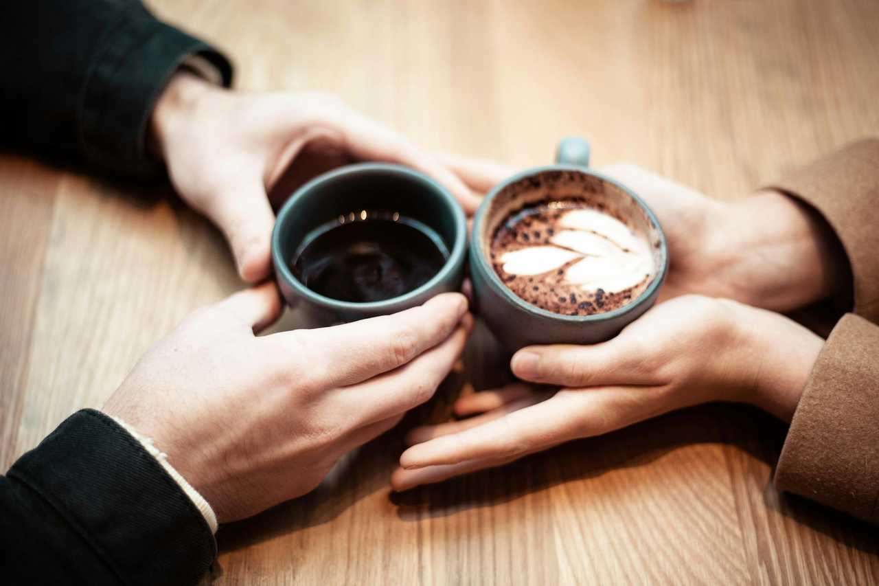 couple on a date holding their coffee and their hands together over the table