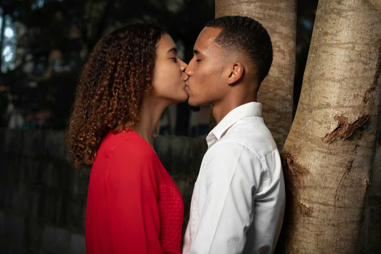 woman and man kissing on their first date by a tree