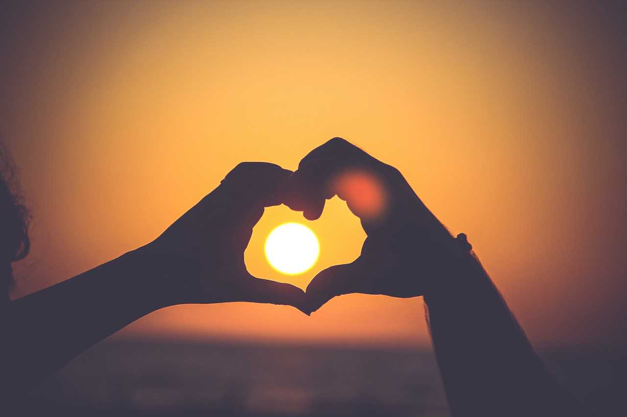 hands making the shape of a heart in the sunset