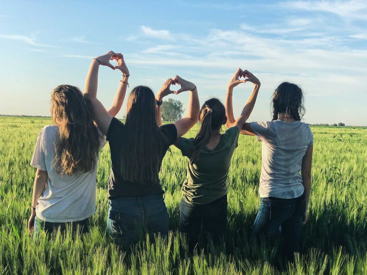 friends making heart shapes with their hands standing on a tall grass field on valentine's day