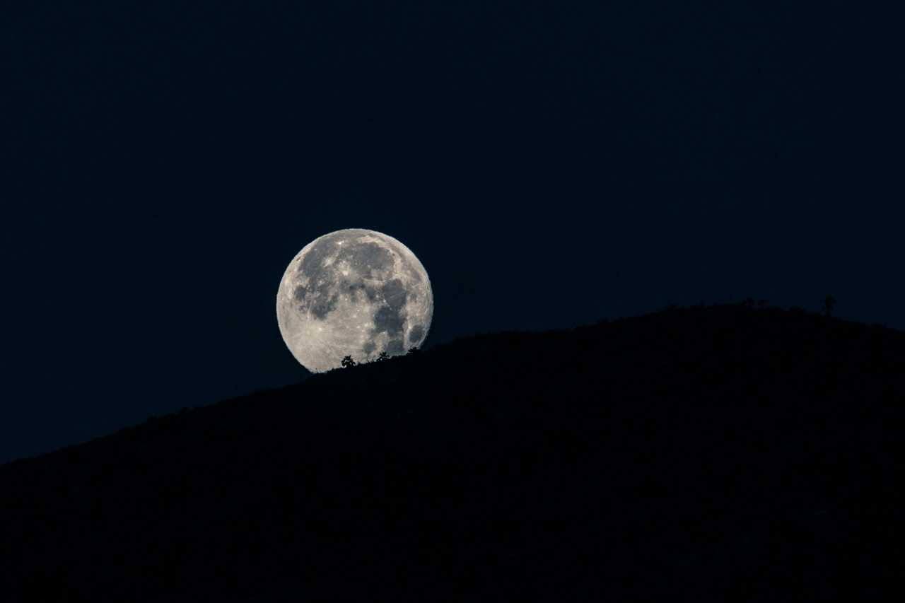 view of the moon in the sky behind a hill in the dark for good night messages