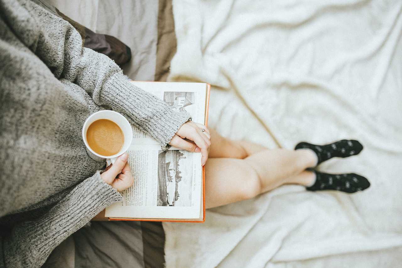 woman with book and cup of coffee in hand at bed getting good morning wife messages