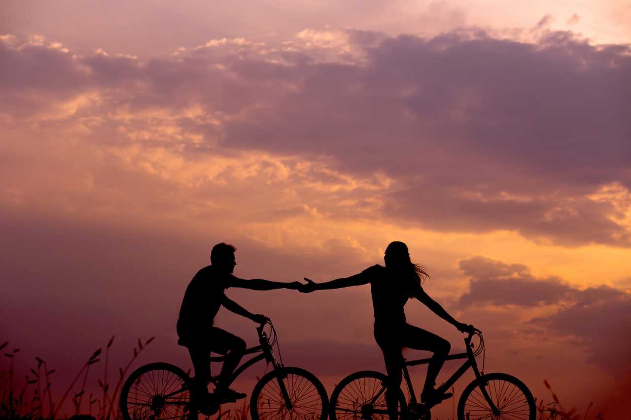 boyfriend and girlfriend riding bikes holding hands in the dusk