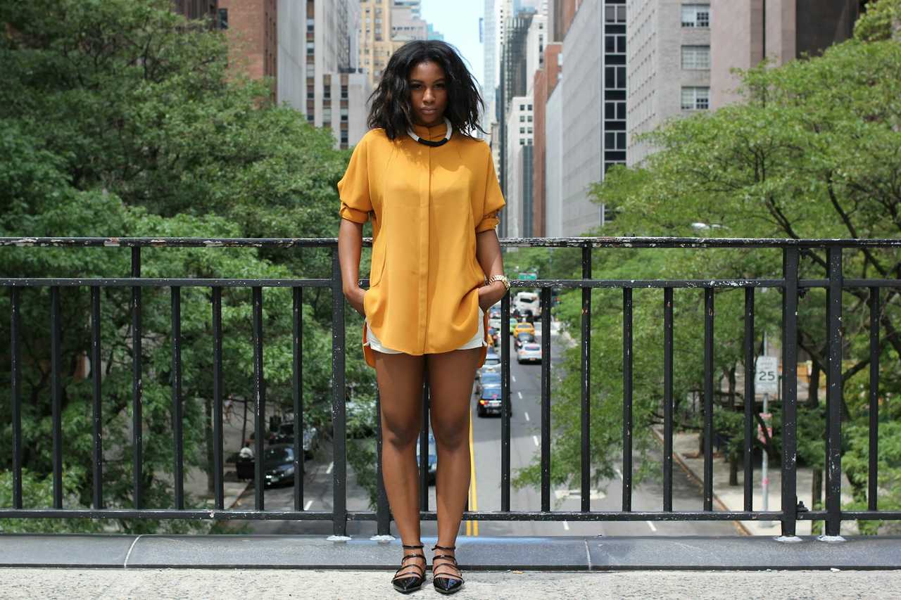woman wearing yellow and standing in a bridge over a avenue in a big city getting morning texts for her