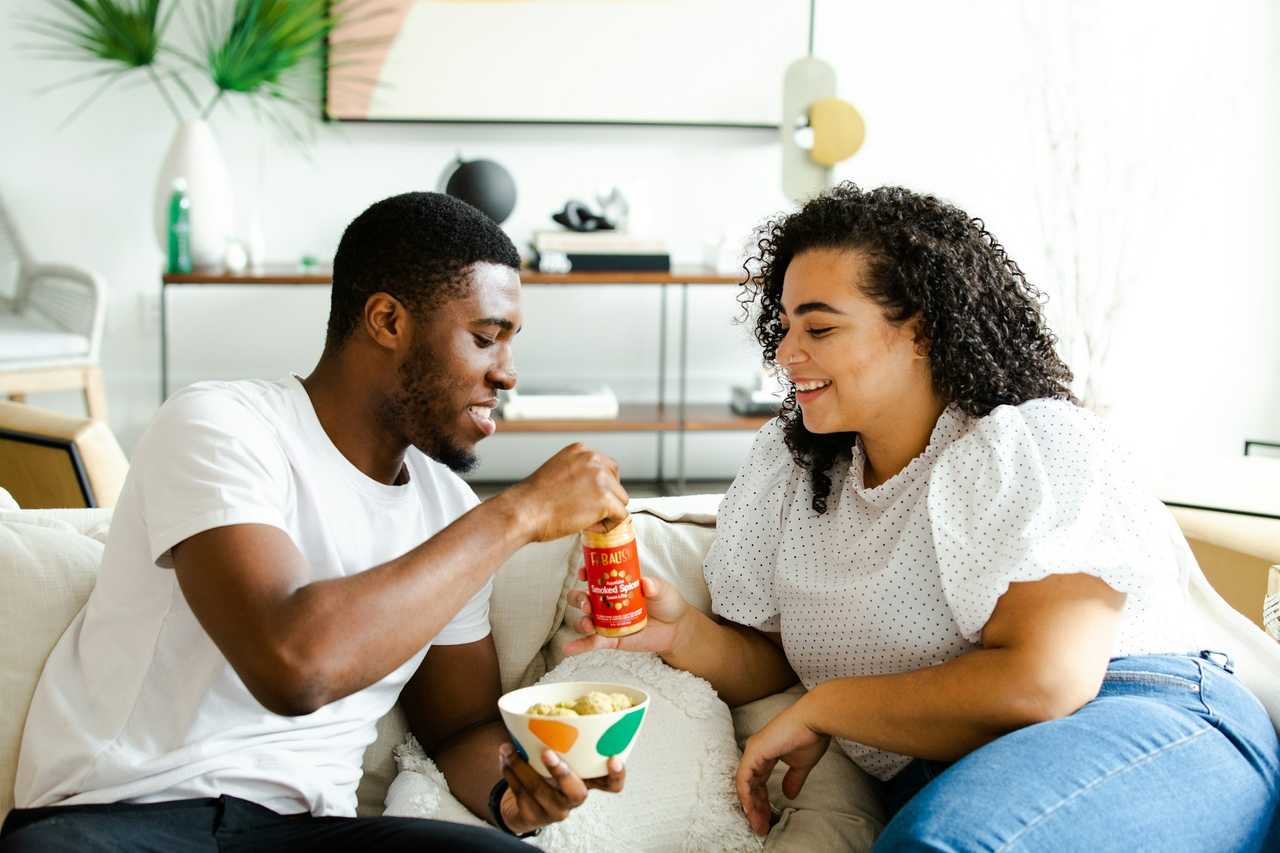 couple sharing snacks on the couch having a date on Valentine's Day after sending Valentine messages for boyfriend