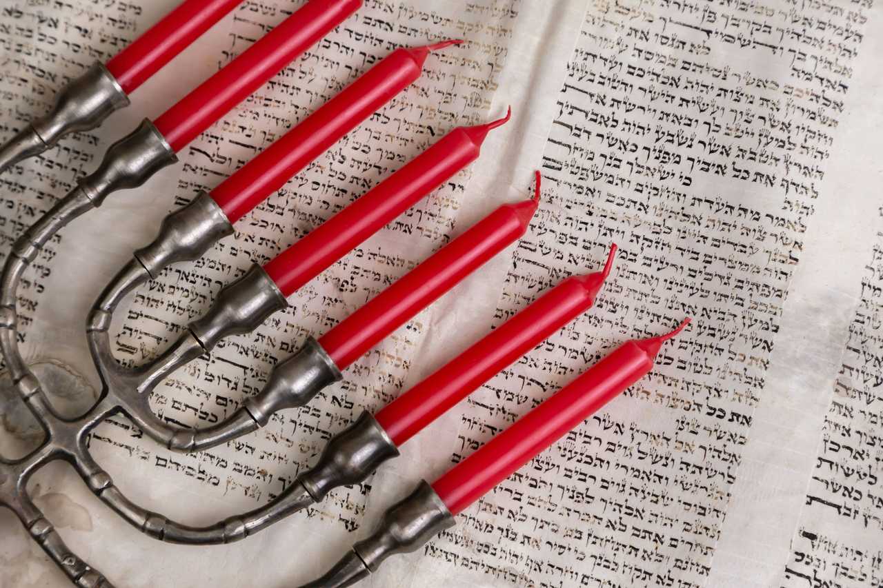 hanukkiah over a torah text in hebrew with red candles for happy greetings