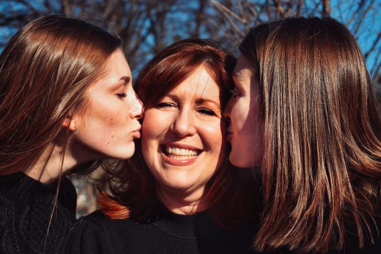 mother being kissed in the cheek by her two teenager daughters for happy mother's day quotes