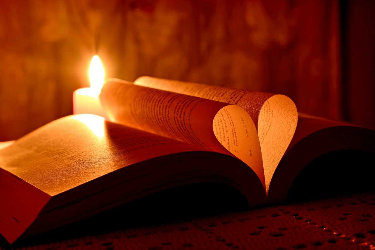book with valentine's day quotes for her making a heart shape with two pages next to a lit candle