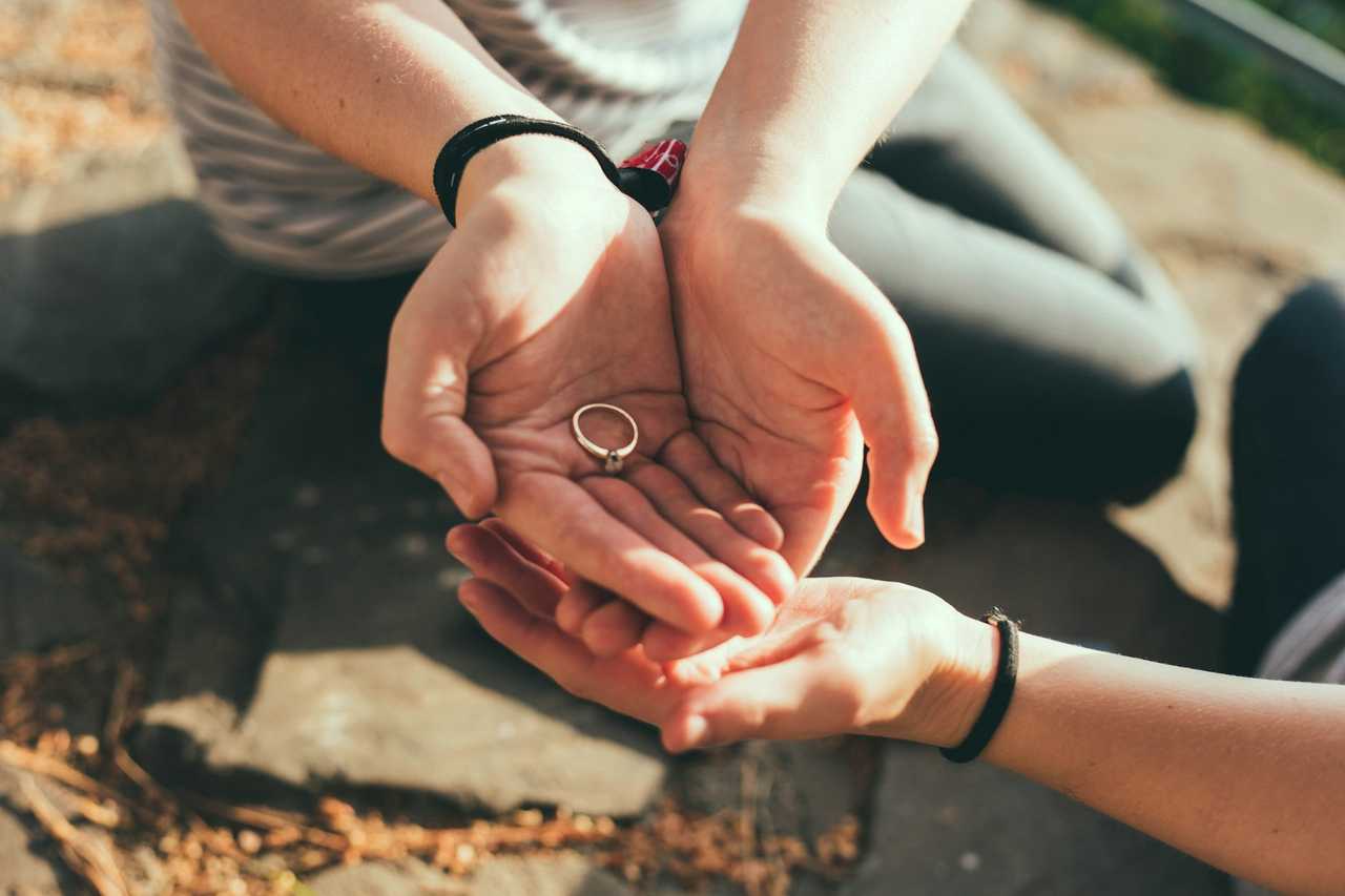 couple holding an engagement ring in their hands in the outdoors