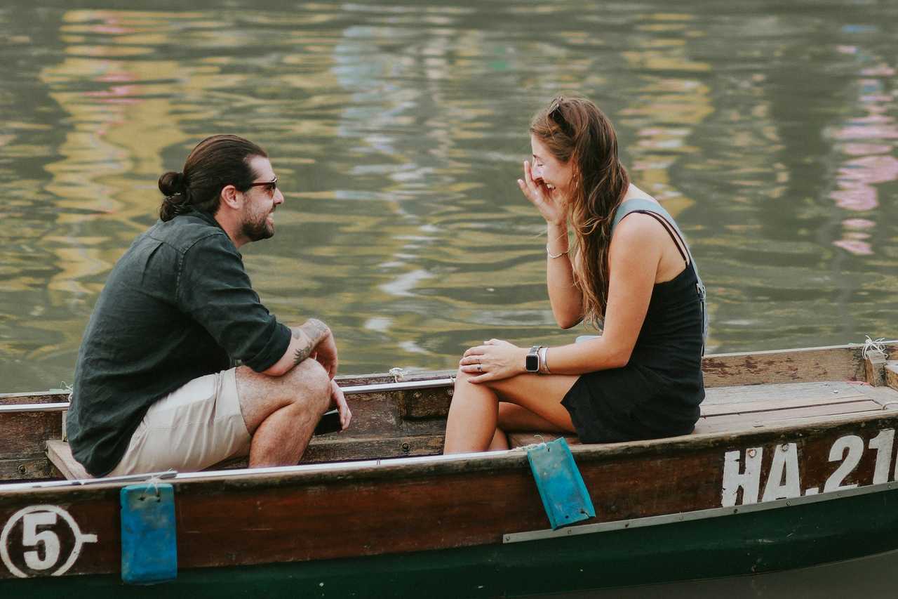 man and woman in a row boat in a lake as a first date talking about hobbies while laughing