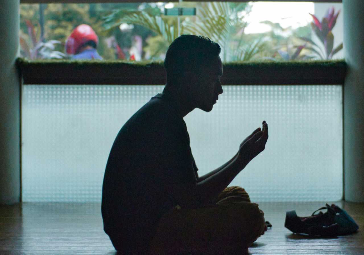 man praying seated in the floor in a dark room from the ai prayer generator