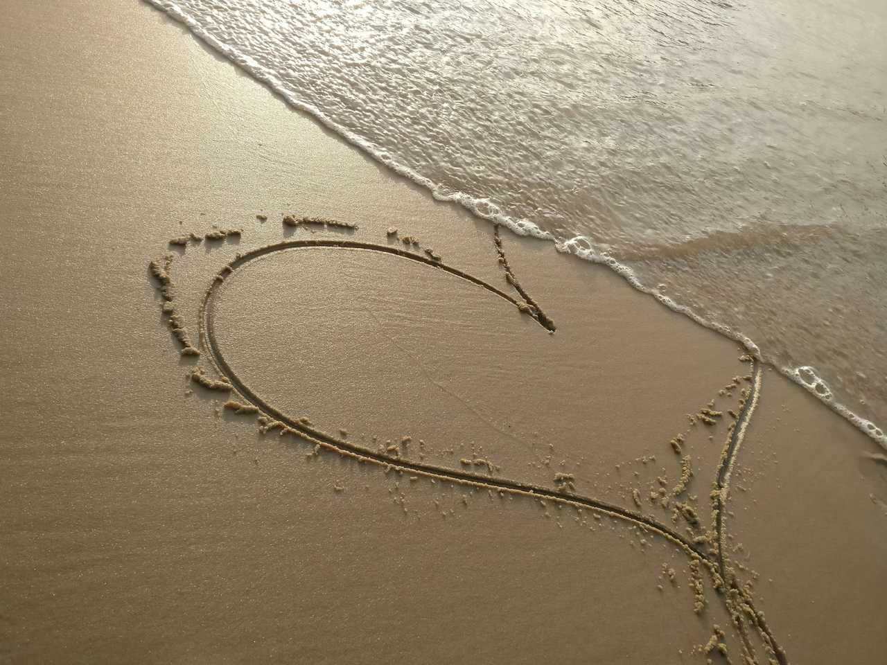 heart drawn in the sand with wave coming to erase it for a love confession gesture