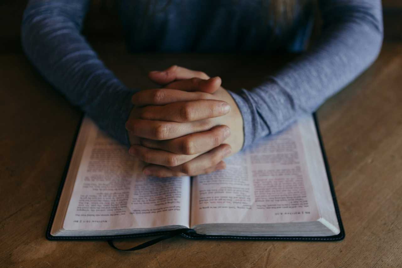 hands together over a Bible praying an ai generated prayer